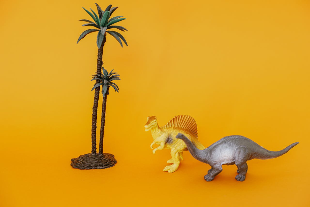 Colorful toy dinosaurs and palm trees on a vivid yellow backdrop, perfect for playful themes.
